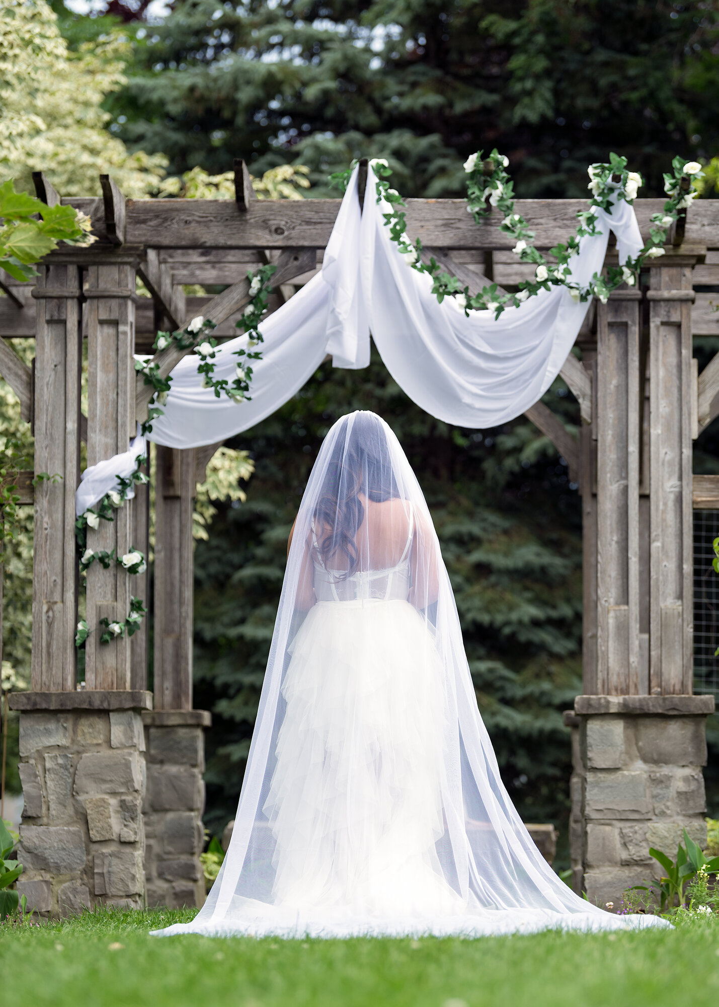 Veiled bride standing beneath a garden arbor in Waterloo, Ontario — fine art wedding photography by NN Popa